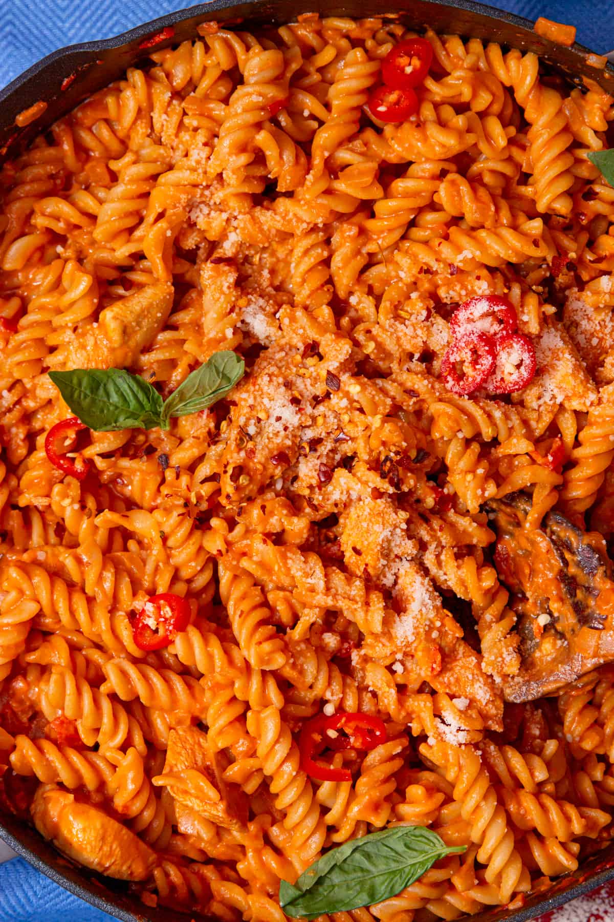 Tomatoey, saucy fusilli pasta with chicken in a pan mixed topped with fresh basil and grated cheese in a pan.