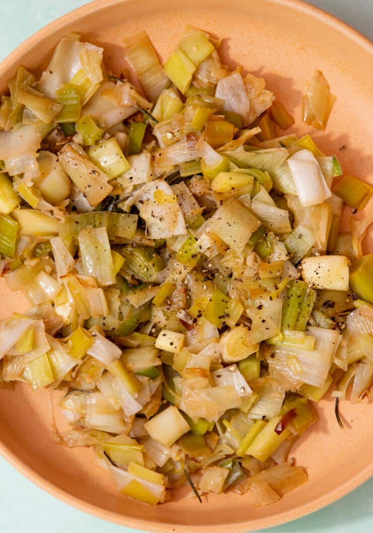 Sauteed leeks in a dish pon a white background.