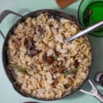 A large pan full of cream pasta shells topped with mushrooms and herbs with a metal spoon in the pan.