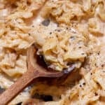 Creamy sliced cooked cabbage in a pan with a wooden spoon.