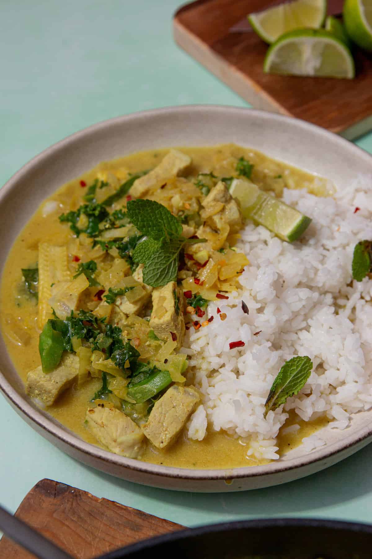 A bowl with rectangular pieces of pork with rice and a curry sauce, topped with fresh mint and a lime wedge.