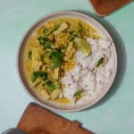 A plate with rice and pork slices in a curry sauce topped with fresh min and a lime wedge.
