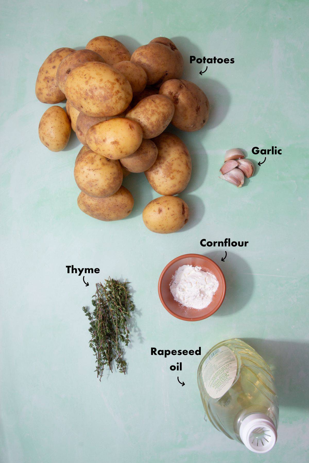 Ingredients to make roast potatoes laid out on a pale blue background and labelled.