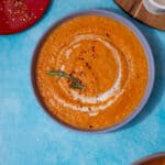 A bowl of orange coloured vegetable soup with a swirl of cream on a blue background.
