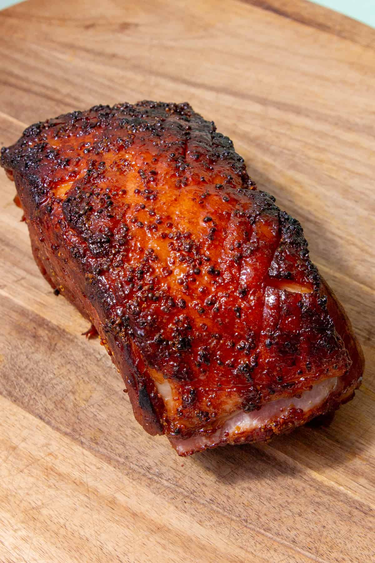 Roasted ham with dark brown glazed topping on a wooden board.