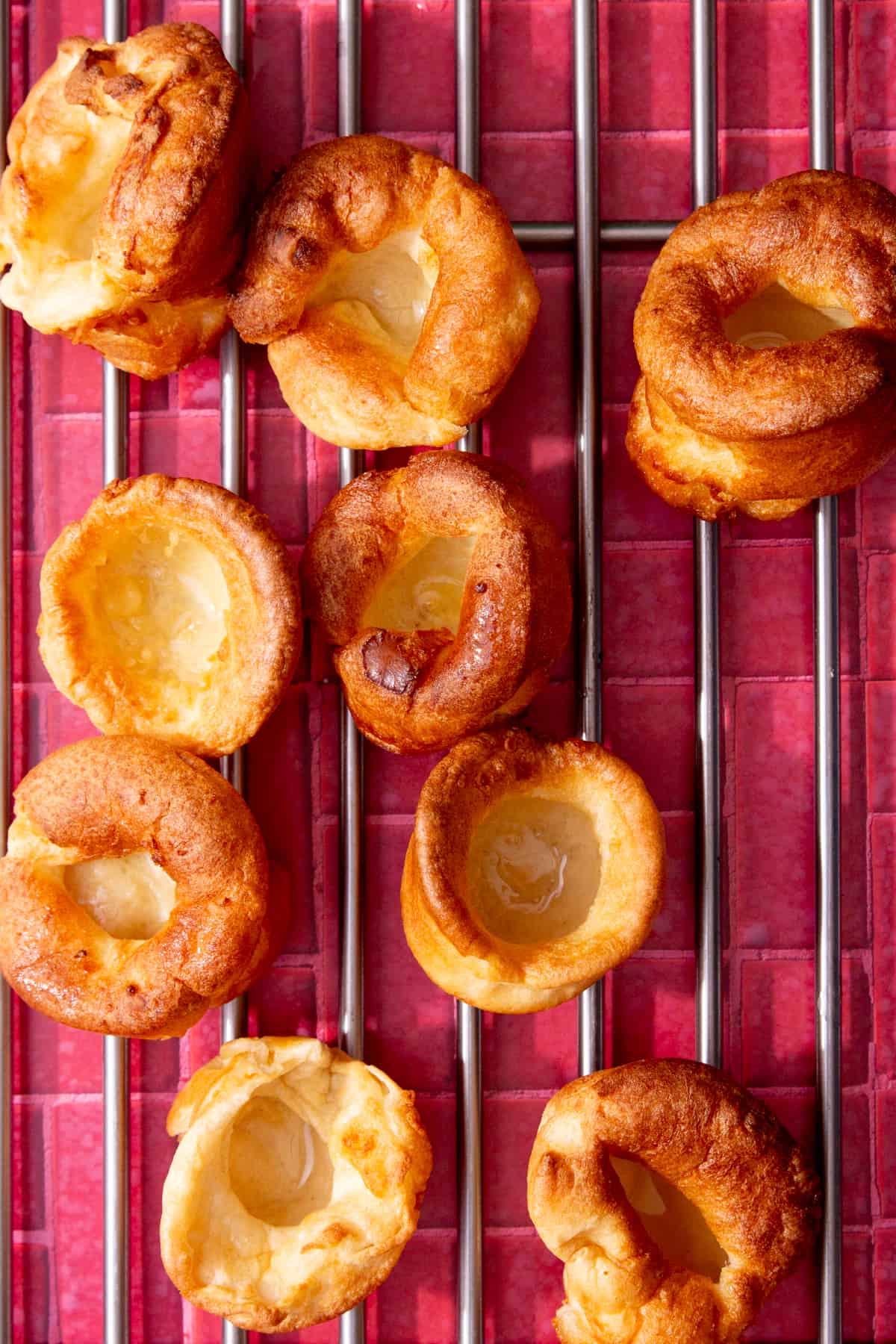 9 round, golden browned Yorkshire puddings on a metal rack of a dark pink background.