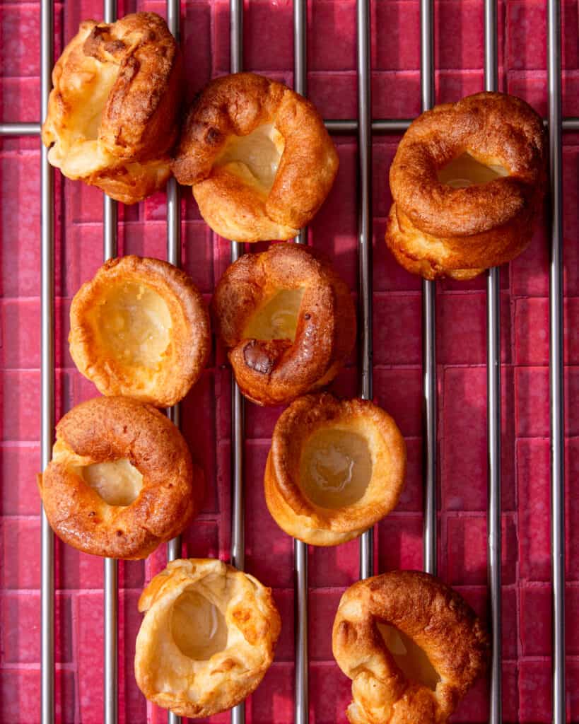 Golden brown Yorkshire puddings laid out on a metal grid on a red tile background.
