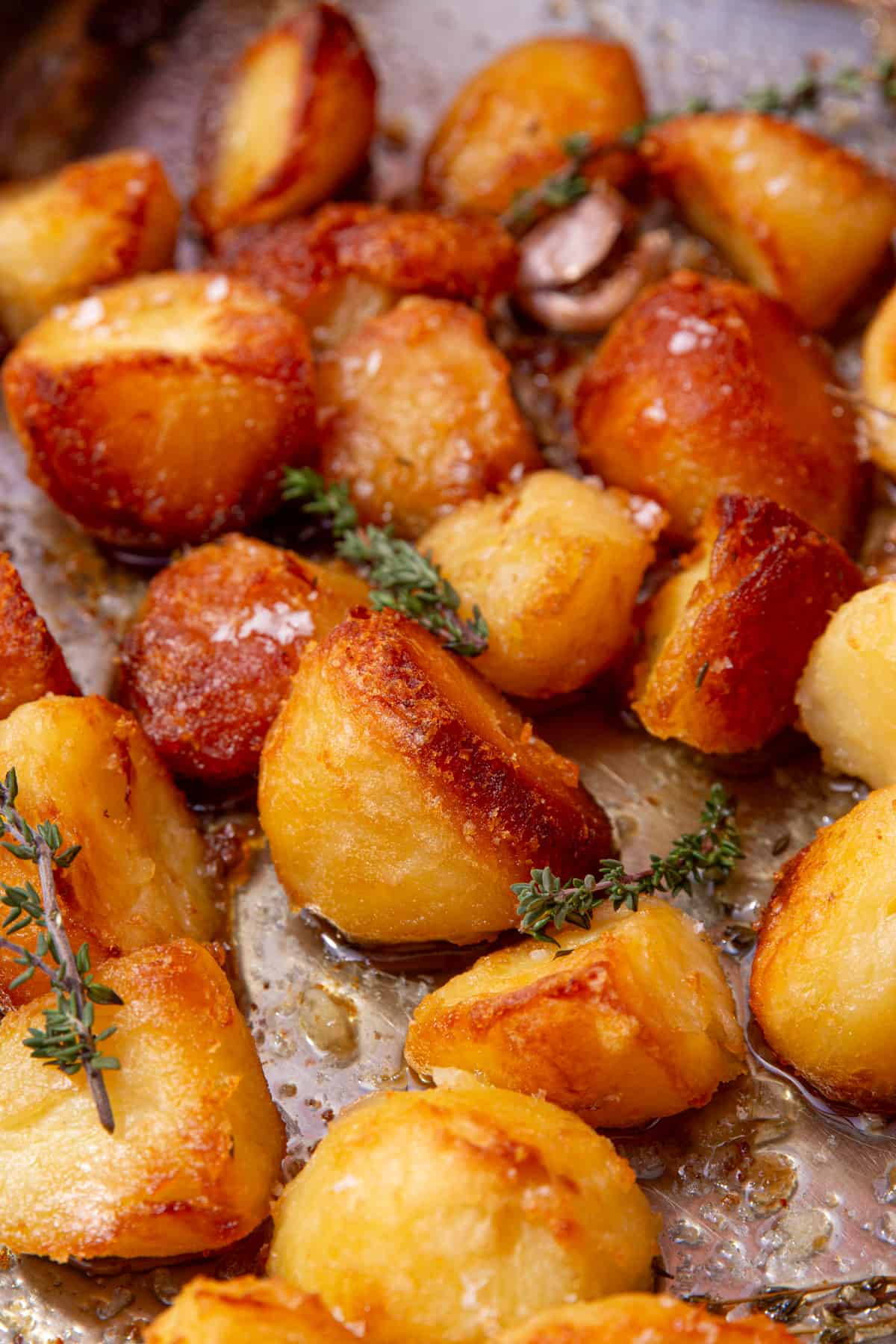 Golden browned roast potatoes on a baking tray with frswsh herbs, salt and garlic.
