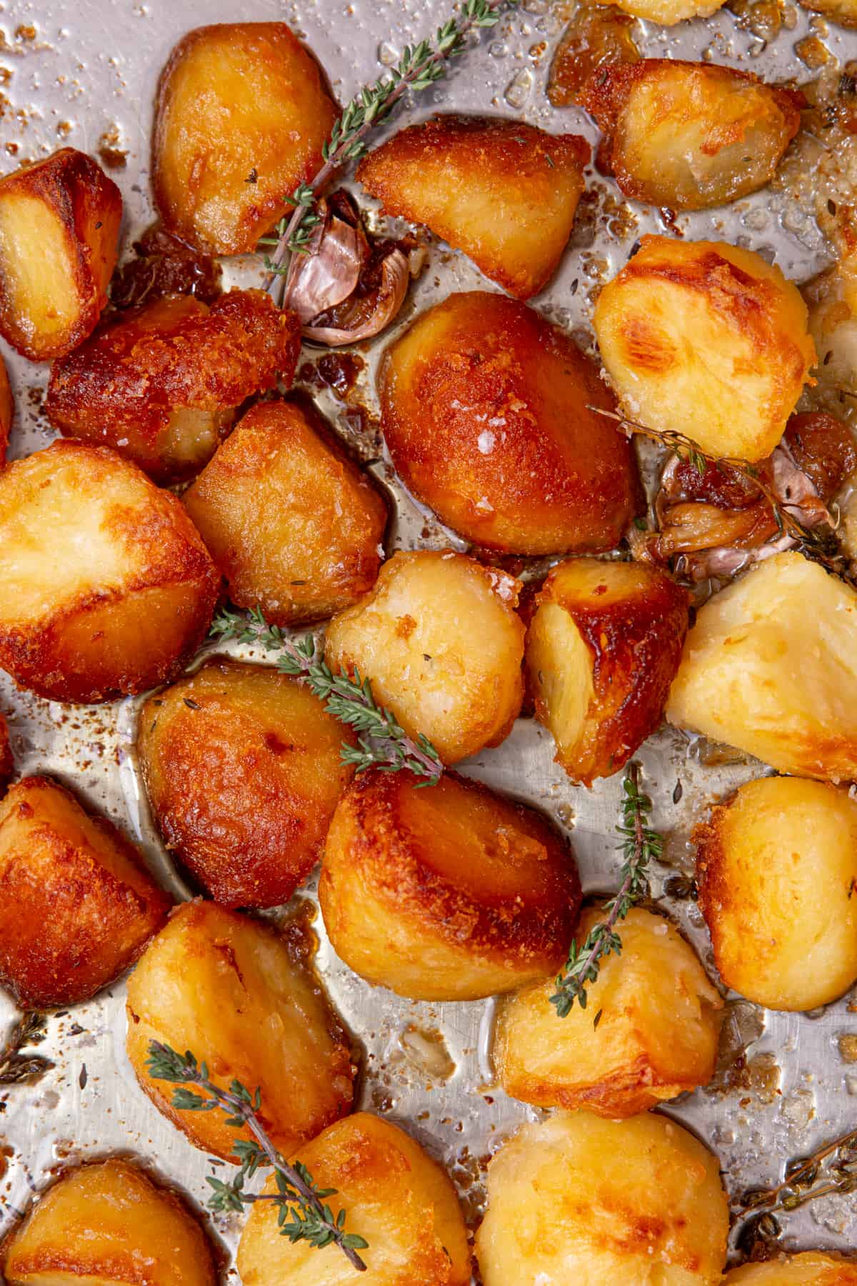 Lots of golden browned roast potatoes on a baking tray with frswsh herbs, salt and garlic.