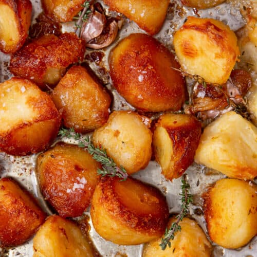 Golden borwned, roasted potatoes in a tray with fresh herbs and garlic.