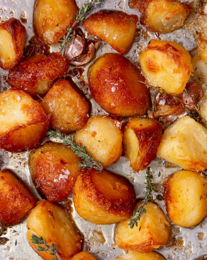 Golden borwned, roasted potatoes in a tray with fresh herbs and garlic.