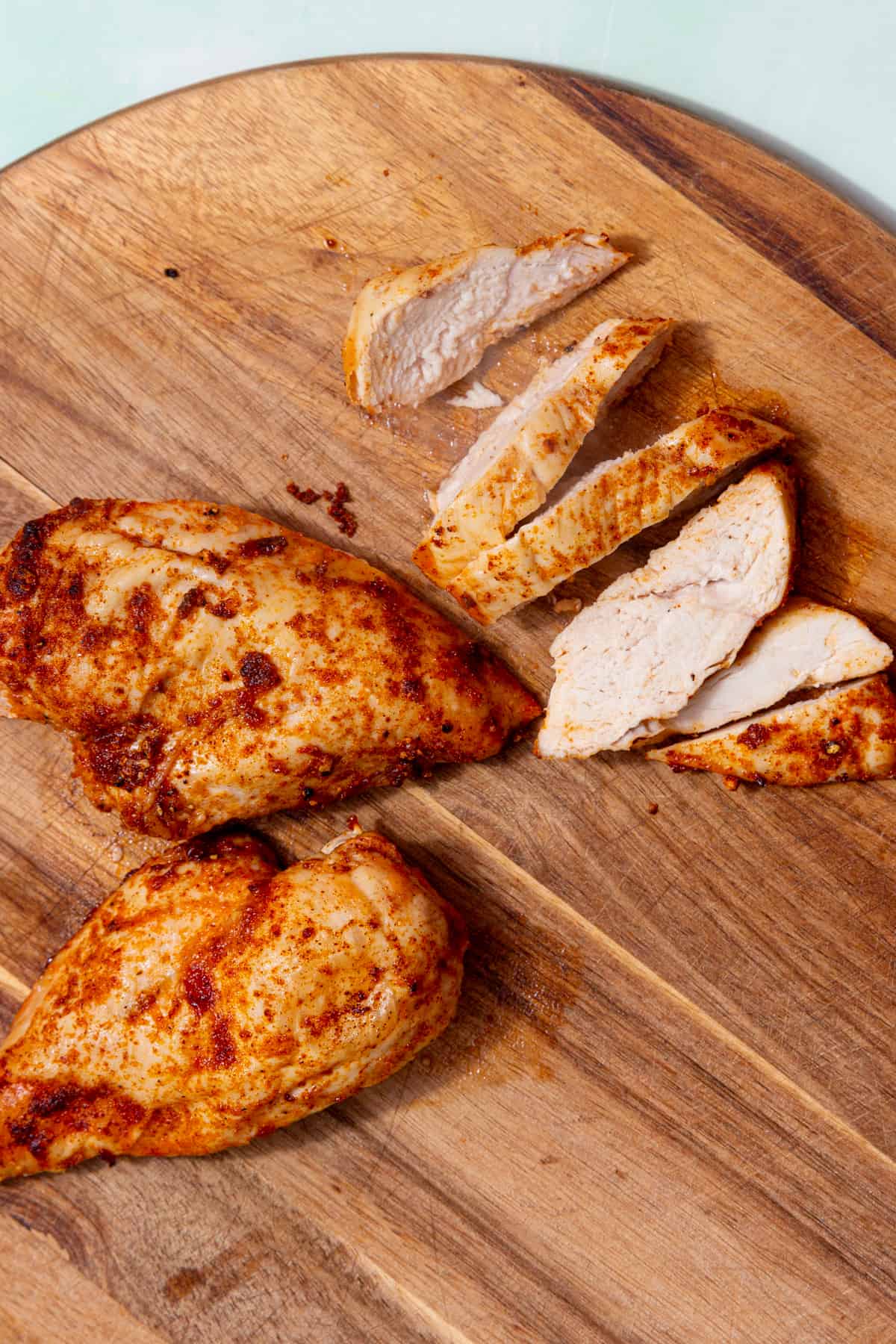 Golden browned, seasoned chicken breast fillets on a wooden board with one piece sliced.