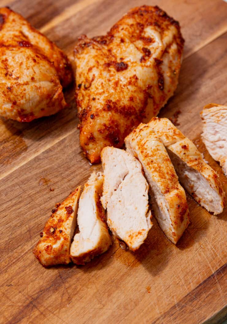Golden browned chicken breast fillets on a wooden board with one piece sliced.