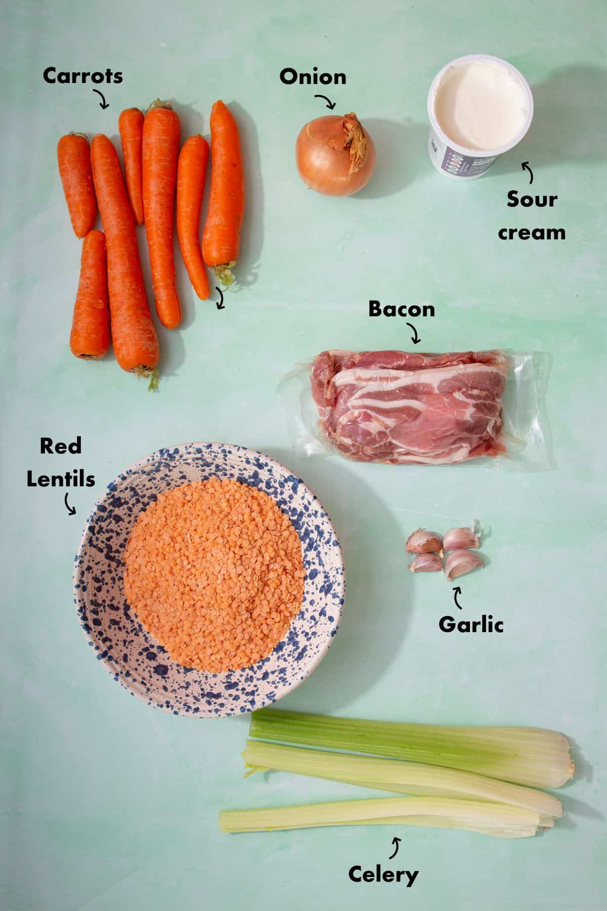 Ingredients to make bacon and lentil soup laid out on a pale blue back ground and labelled.
