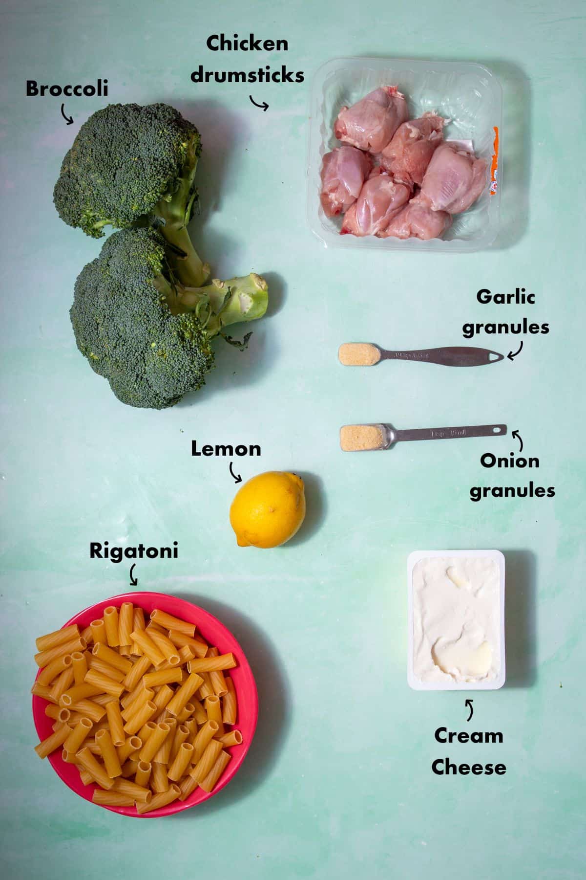 Ingredients to make the chicken and broccoli pasta laid out on a plain blue background and labelled.