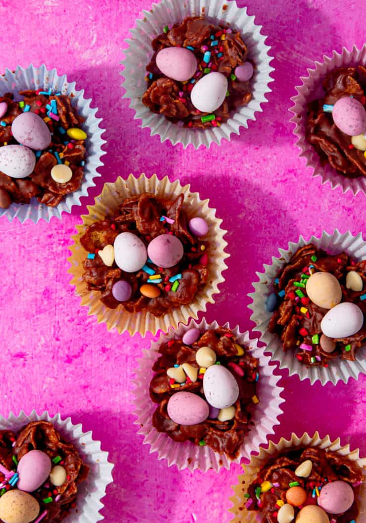 Lots of chocolate cakes with mini Easter eggs decorated on top on a bright pink background.