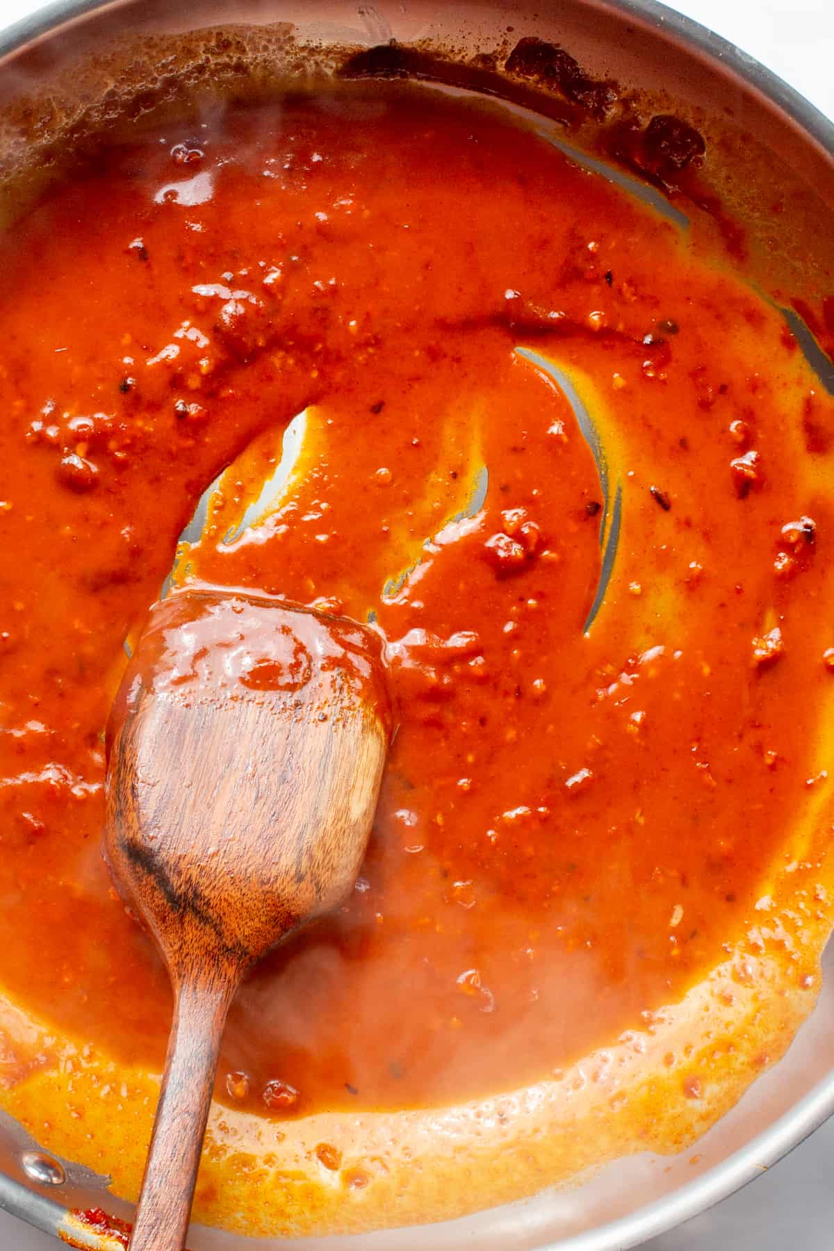 A large pan with bright red sauce bieng mixed with a wooden spoon.