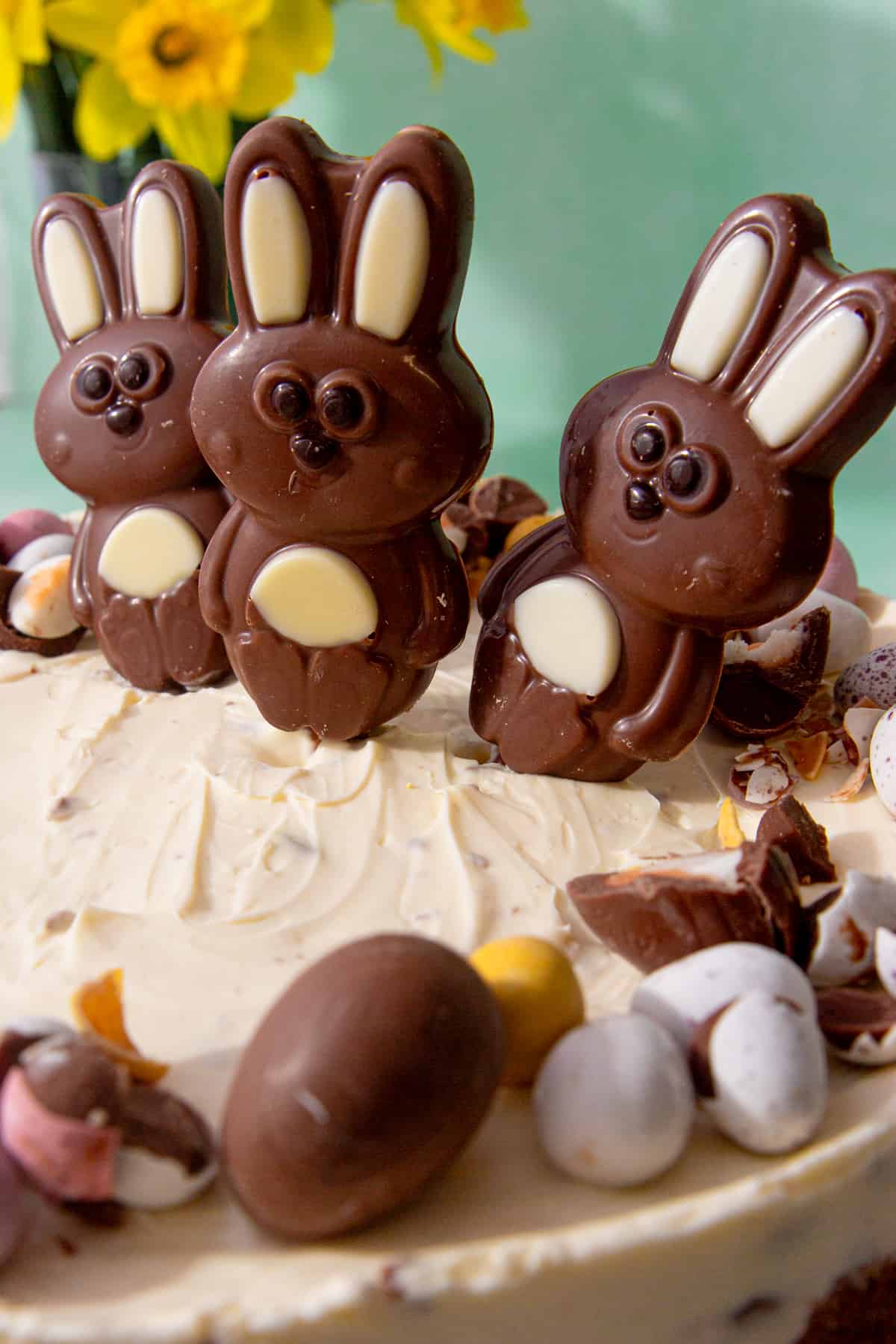 3 chocolate bunnies on a cheese cake decorated with lots mini chocolate eggs.