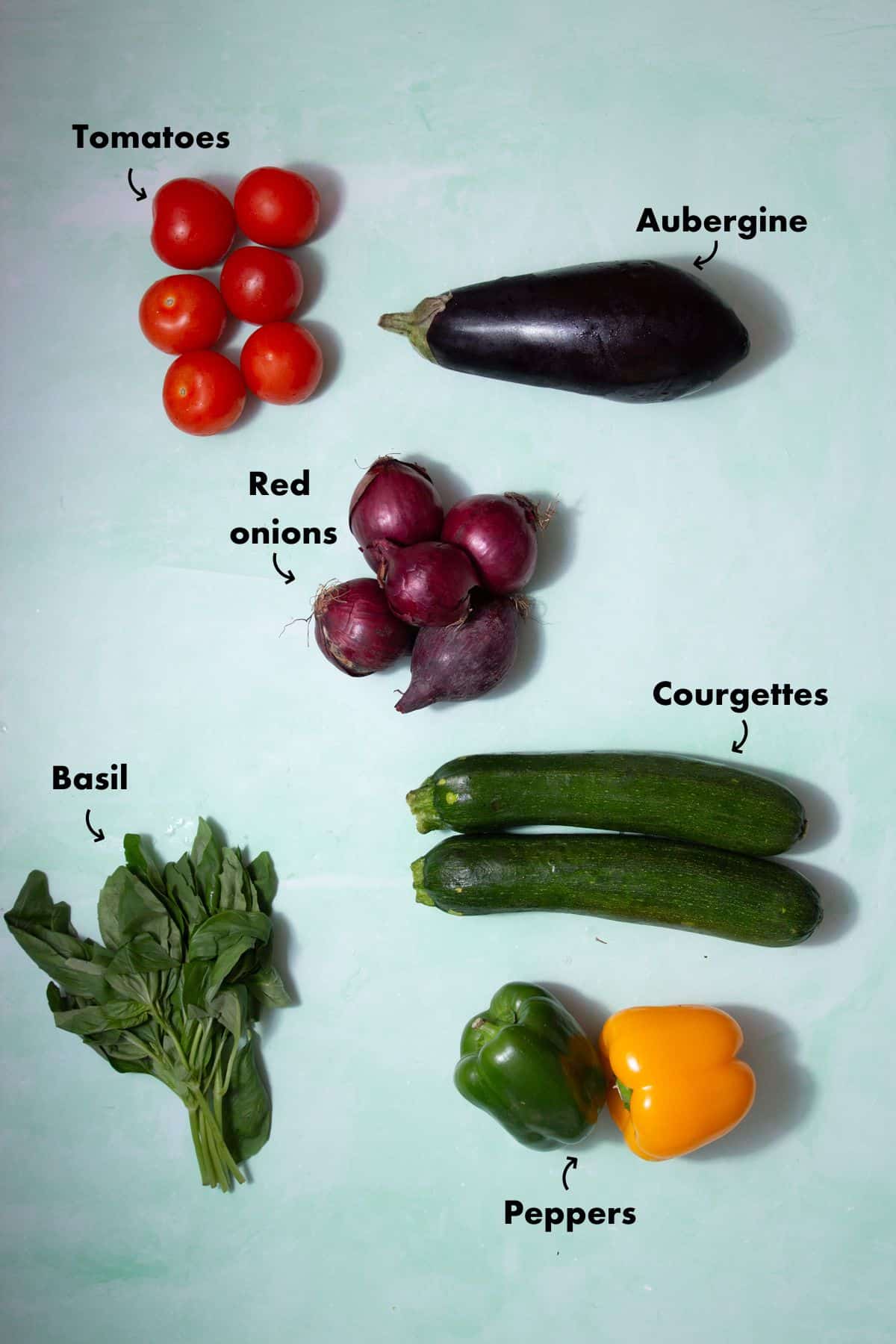 Ingredients to make roasted vegetables laid out on a pale blue background and labelled.