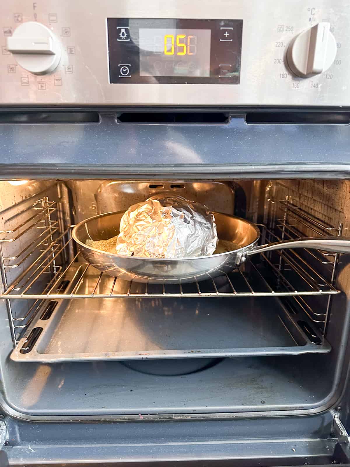 A large pan with a piece of meat covered in foil place on a shelf in the oven.