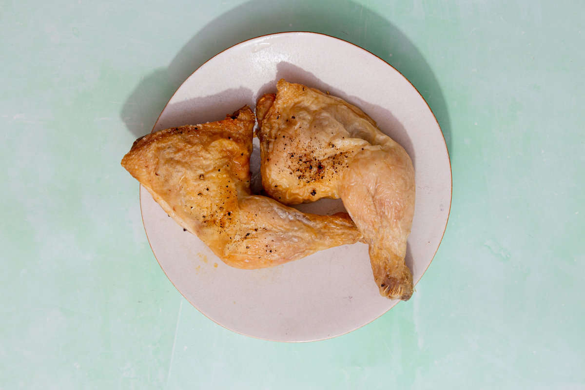 2 cooked and lightly browned chicken legs on a white plate on a pale green background.