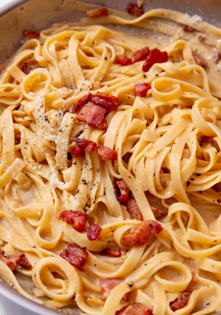 A pan full of tagliatelle with creamy sauce with bacon and parmesan topping.