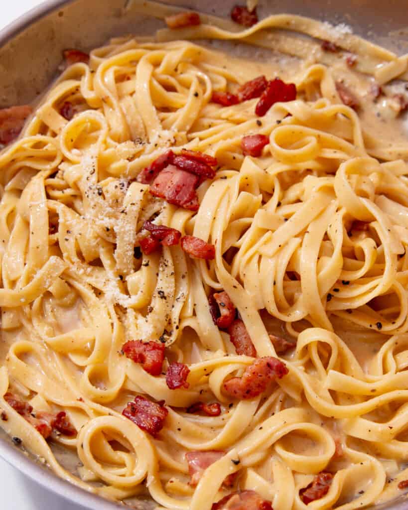 A pan full of tagliatelle with creamy sauce with bacon and parmesan topping.