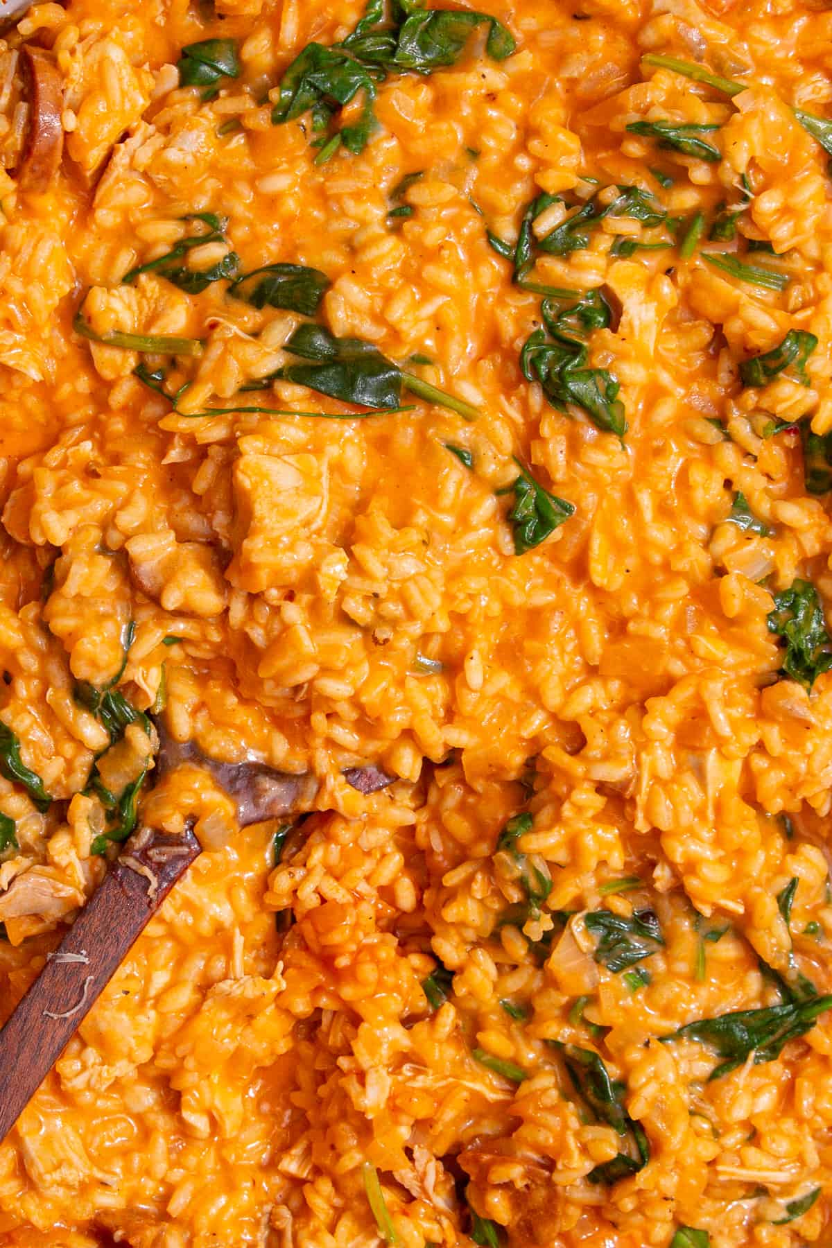 Risotto with pieces of chorizo, chicken, and spinach stirred with a wooden spoon.