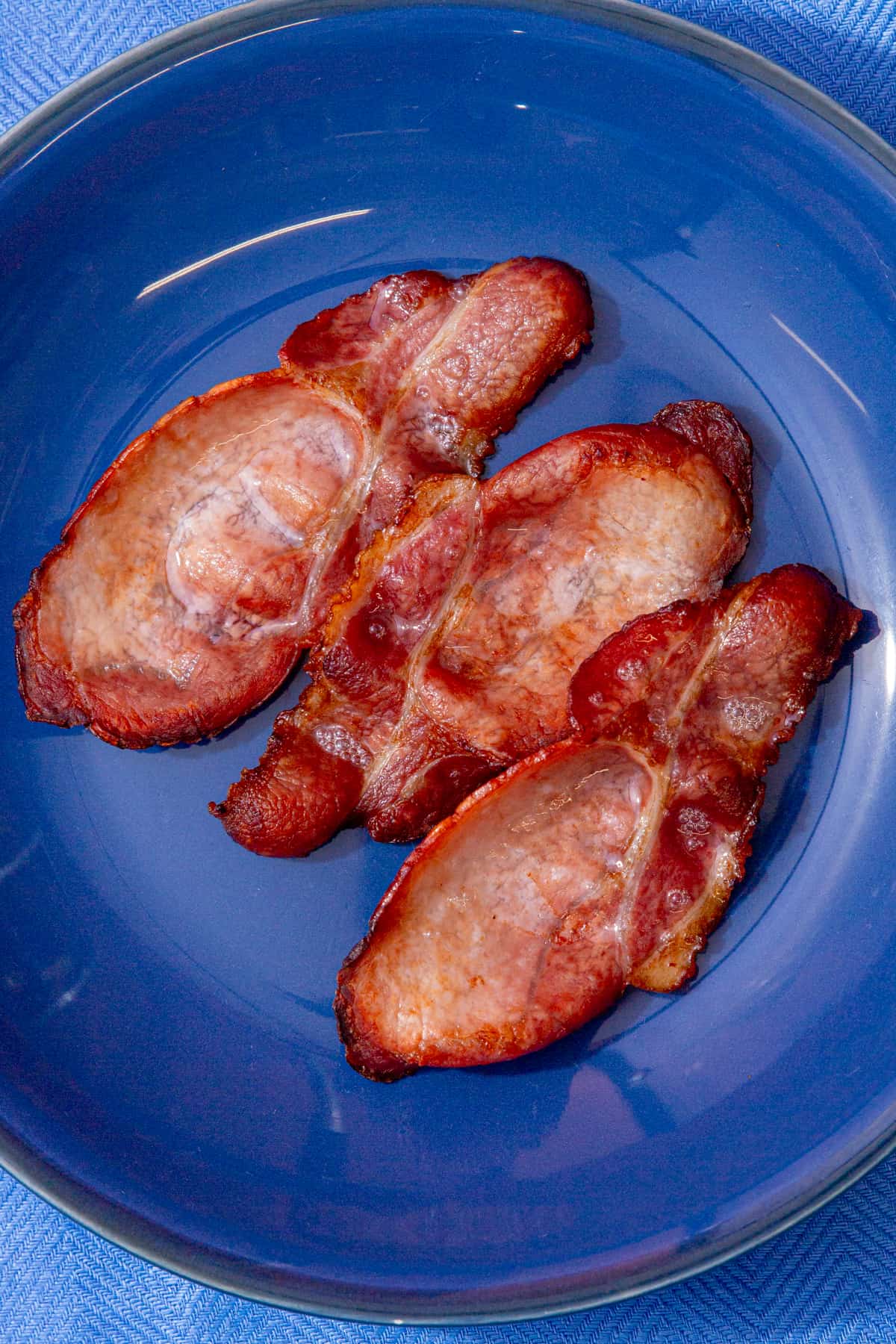 3 cooked and browned bacon rashers on a blue plate.