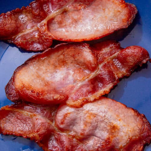 3 rashers of cooked, browned lean bacon on a blue plate.