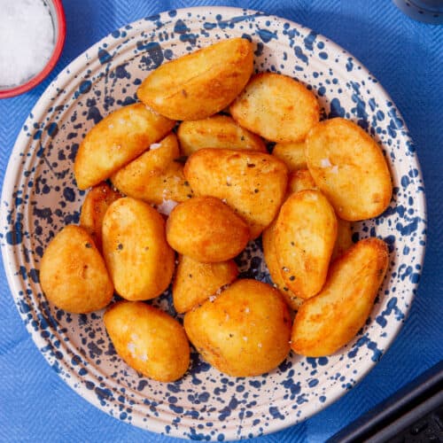 Golden browned roast potatoes in a patterned white and blue bowl on a blue background.