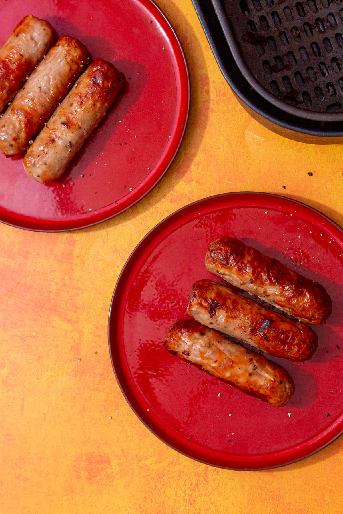 2 red plates with 3 cooked, browned sausages on each plate.