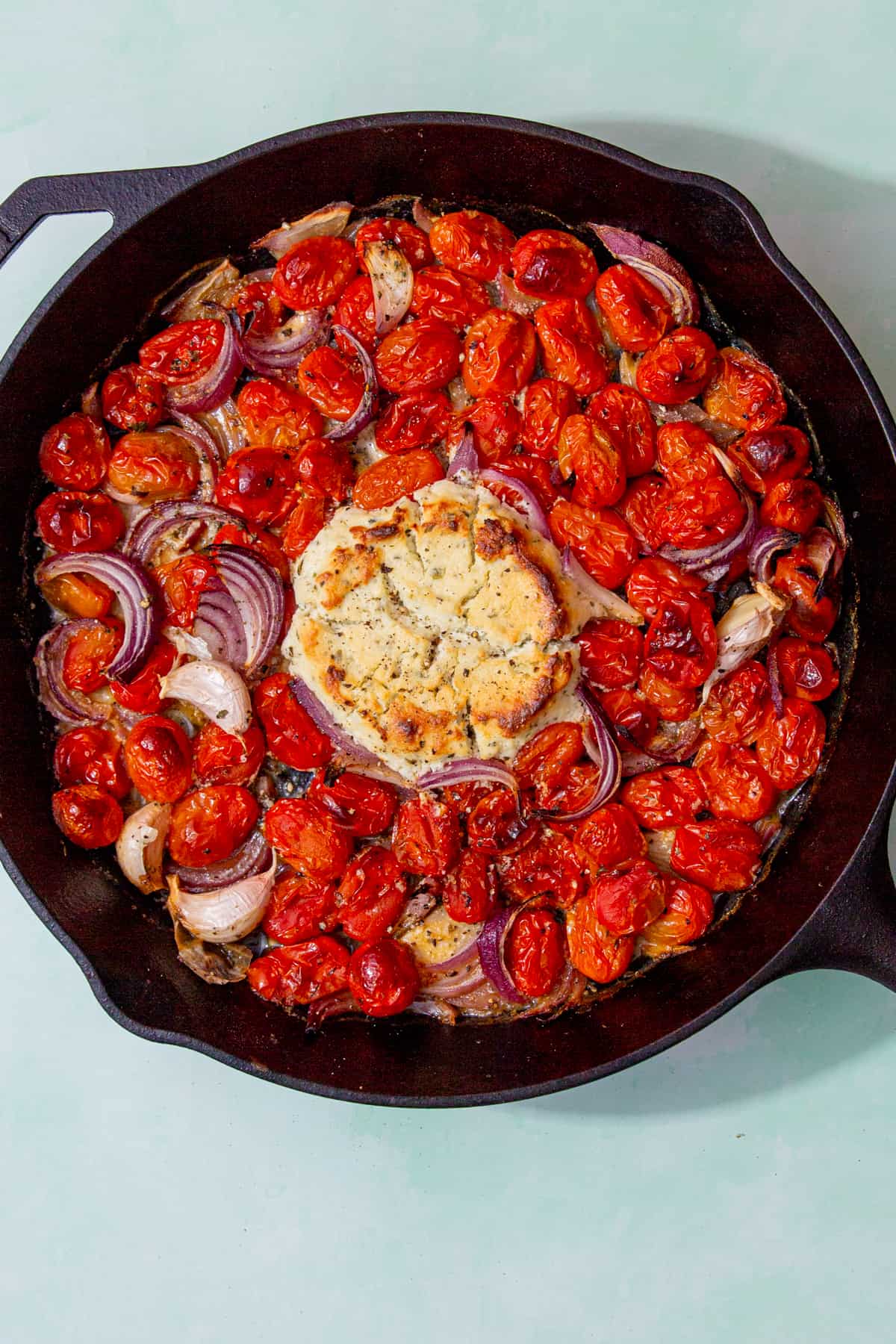 A skillet pan with roasted cherry tomatoes, red onion and roasted soft cheese centre.