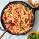 A large pan with pasta in a cheesy sauce, with cherry tomatoes and fresh basil next to a pack of Boursin cheese and fresh basil.