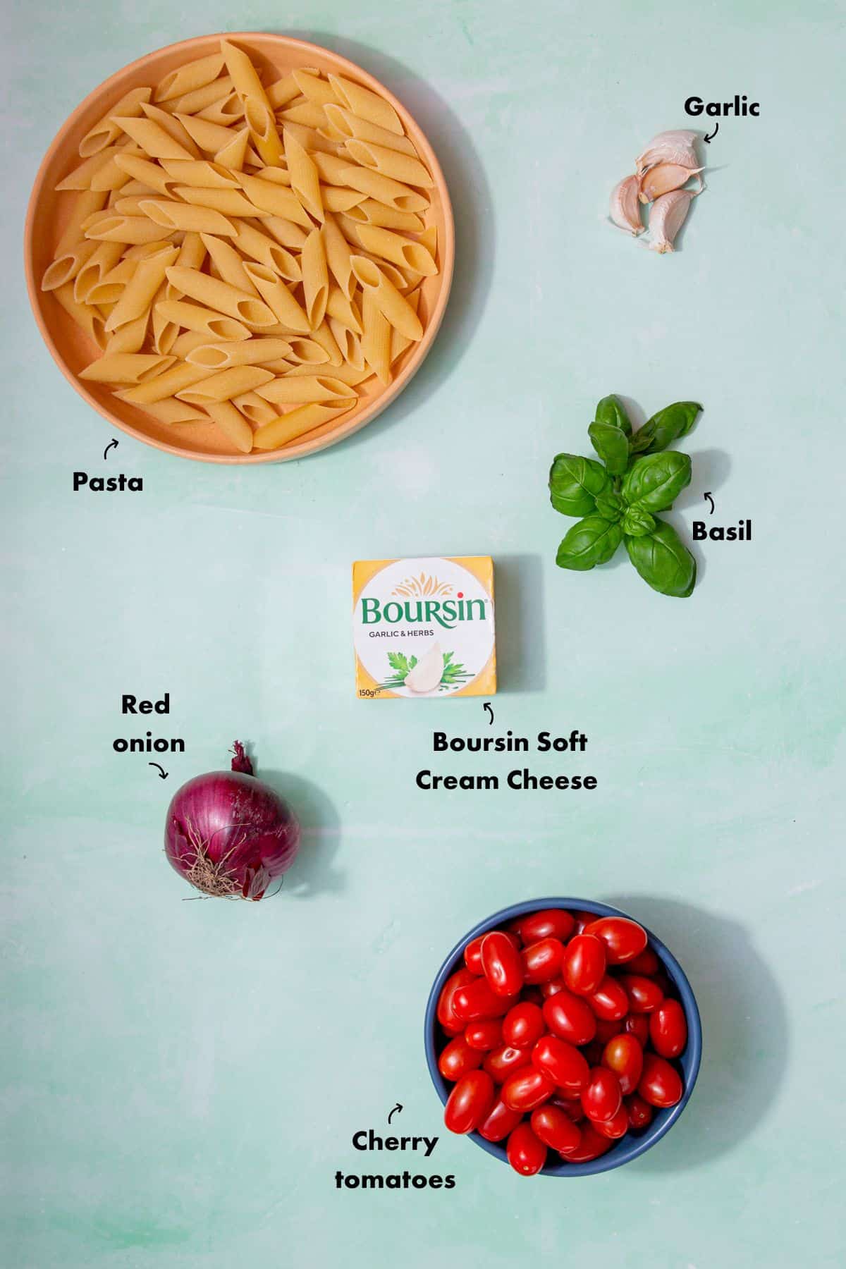 Ingredients to make the pasta with Boursin, fresh basil, red onion and cherry tomatoes laid out on a pale blue background and labelled.