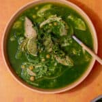 Green soup in a bowl, with chicken, rice and chillies and a wedge of lime.