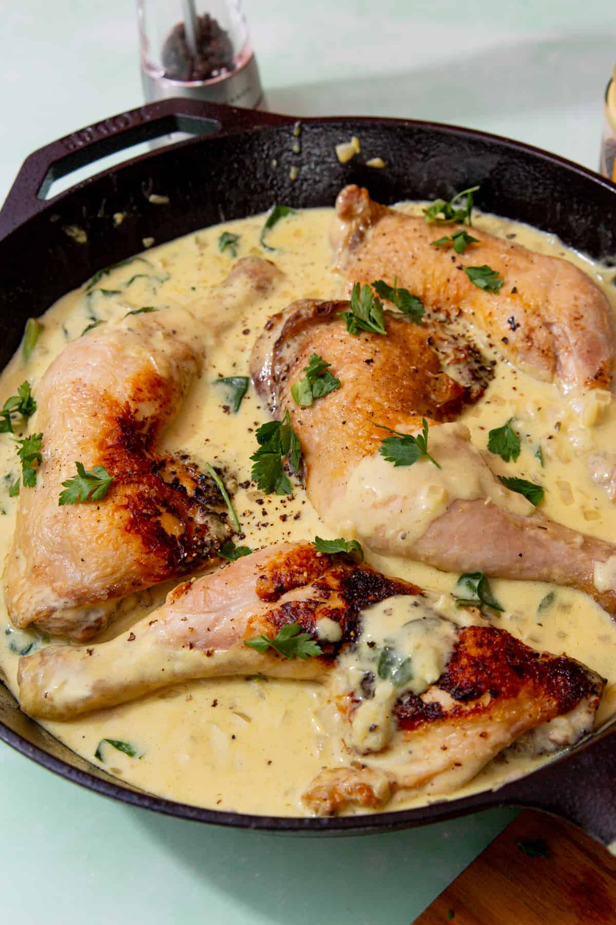 4 golden browned chicken legs with skins in a skillet pan in a creamy sauce topped with fresh parsley.