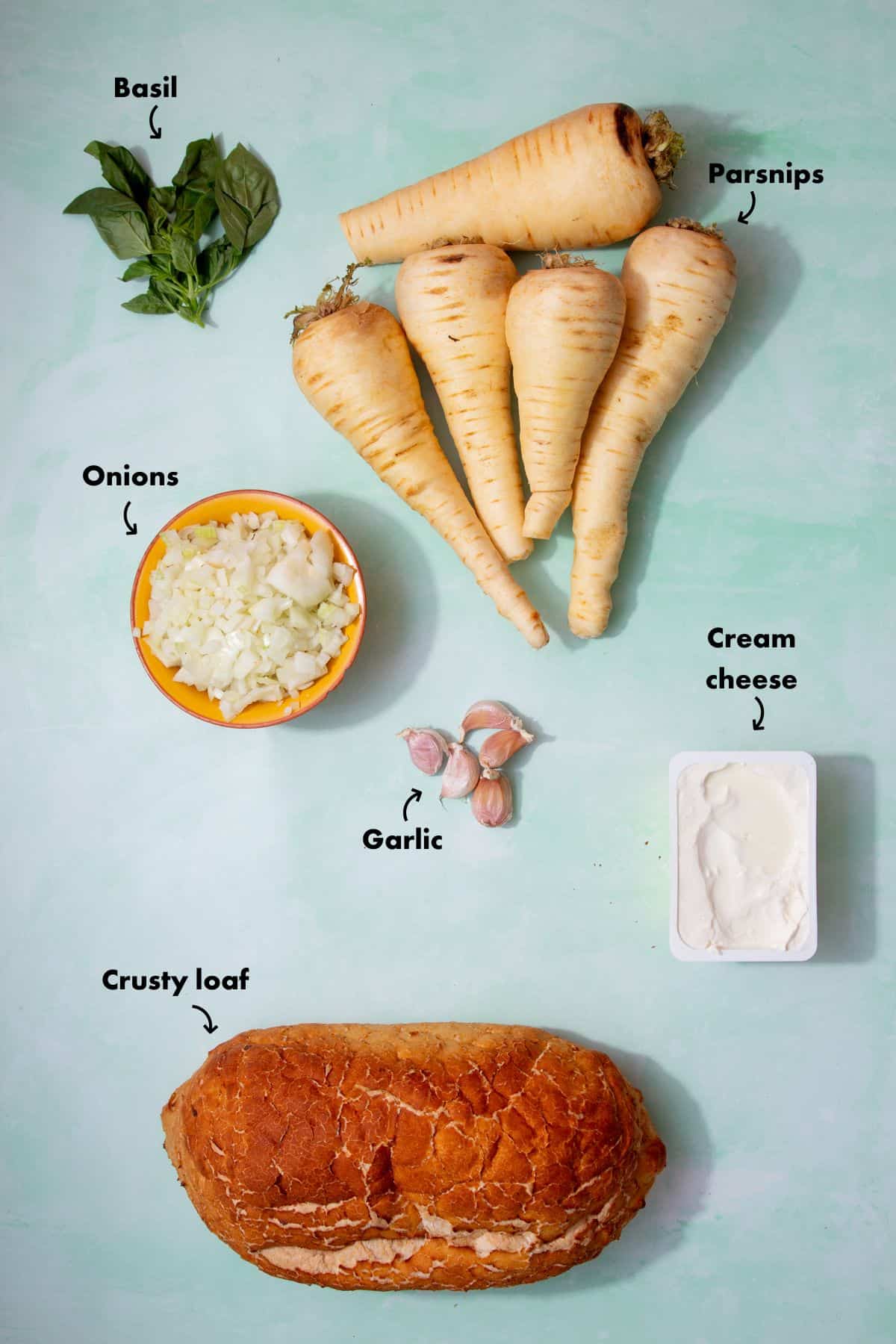 Ingredients to make parsnip soup laid out on a pale blue background and labelled.