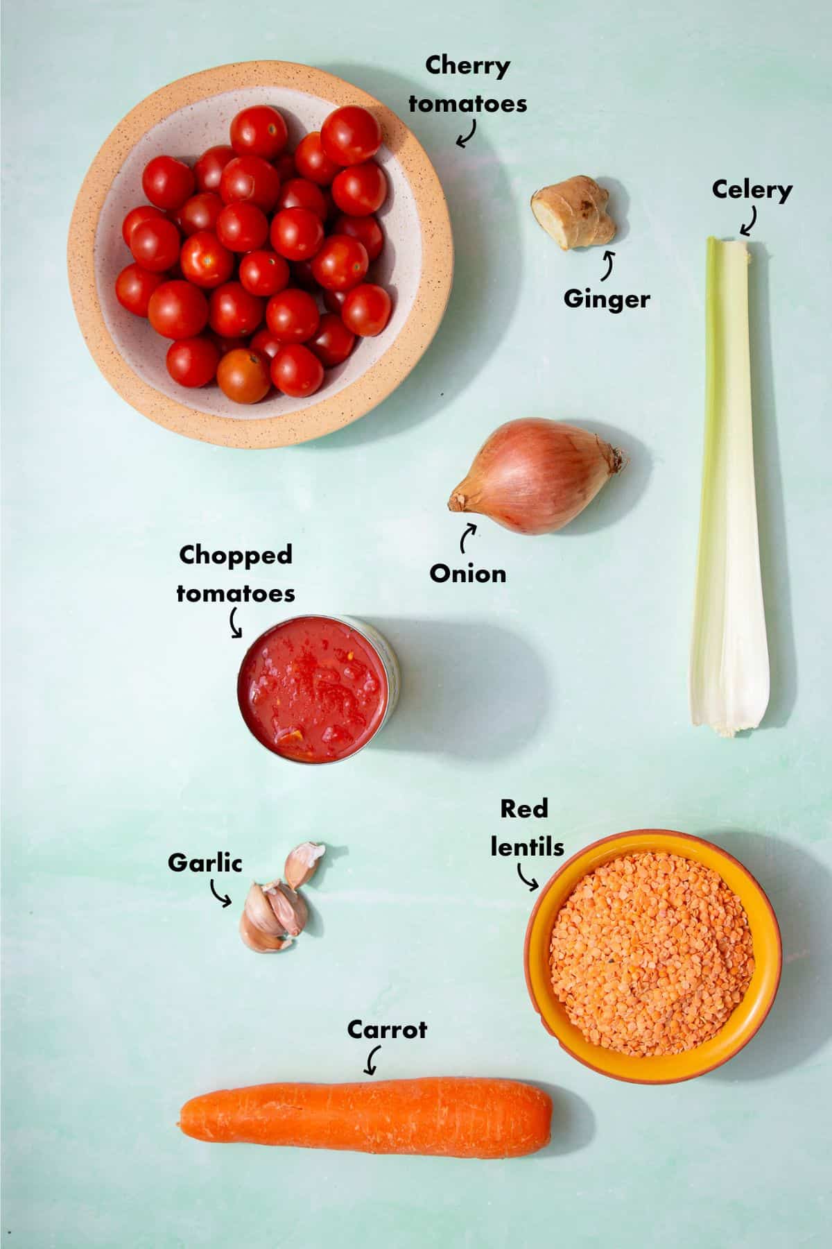Ingredients to make a tomato and lentil soup, laid out on a pale blue background and labelled.