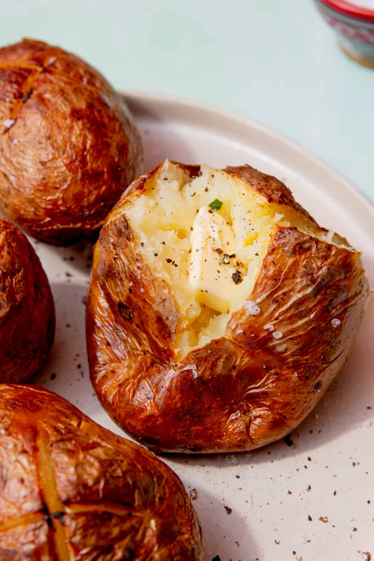 Roasted jacket potatoes on a plate, one opened with a dollop of butter.