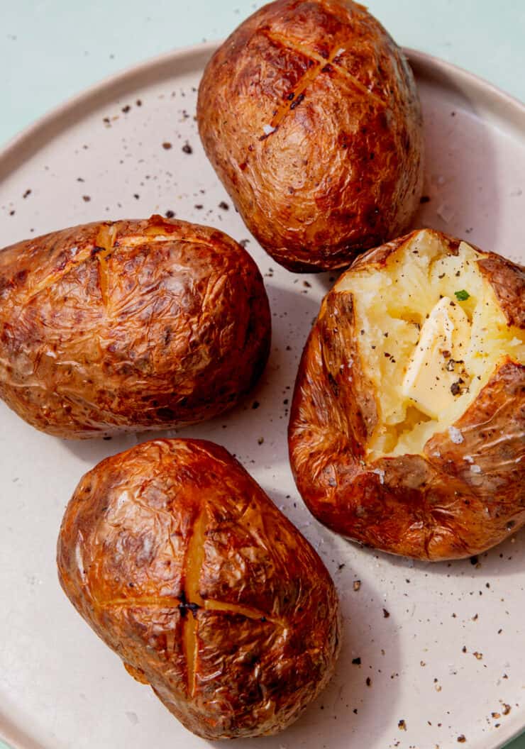 4 cooked jacket potatoes, one opened and with butter in the middle all on a plate.