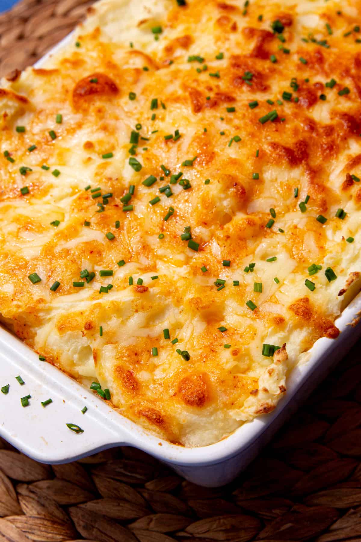 Mash potatoes with golden browned cheesy topping in a white baking dish in partial view.