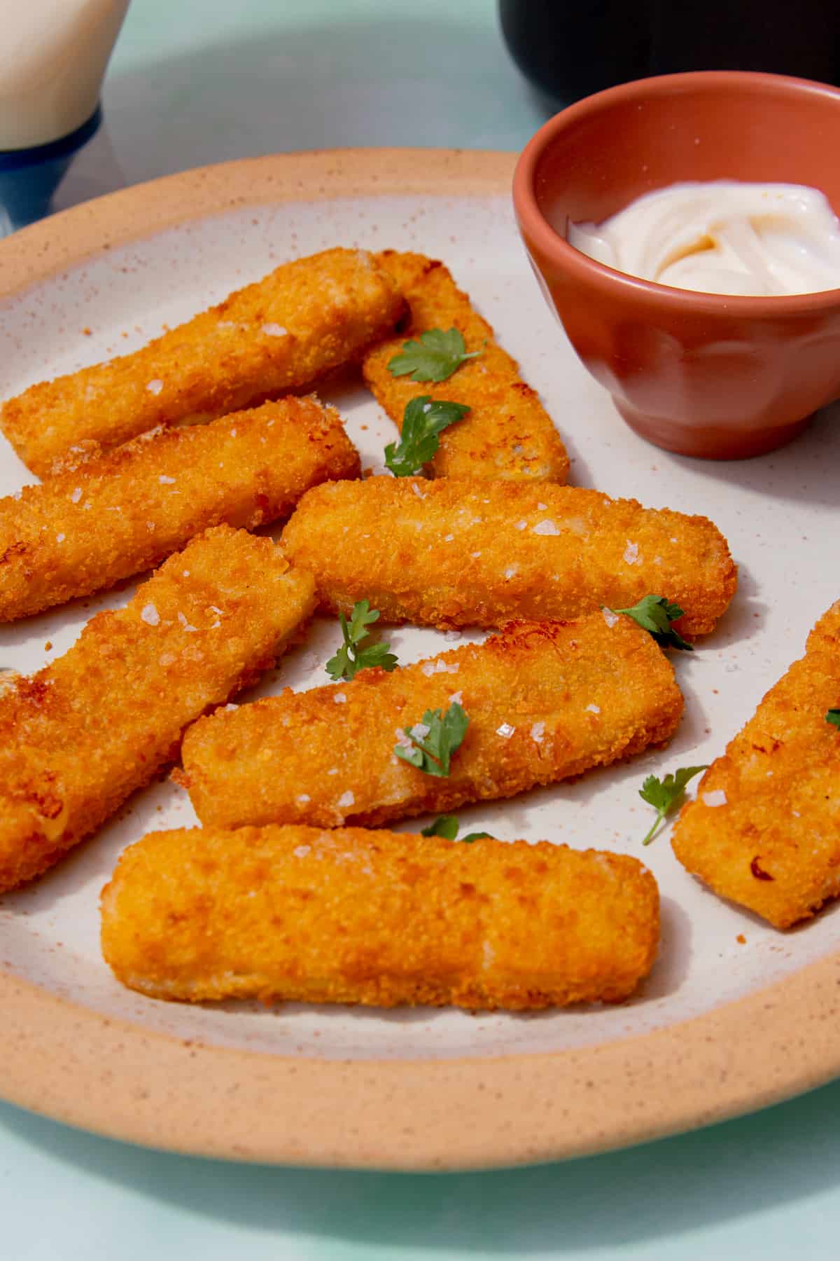 8 fish fingers on a plate topped with parsley with a small bowl of mayonnaise.
