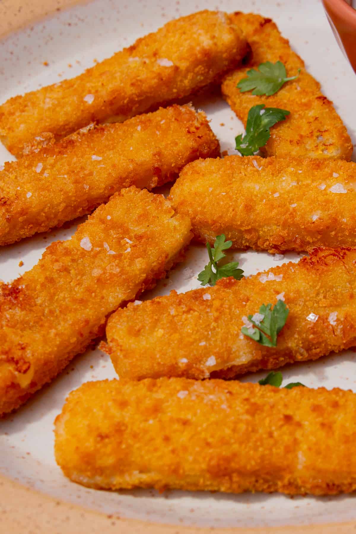7 golden brown battered fish fingers on a plate topped with parsley.