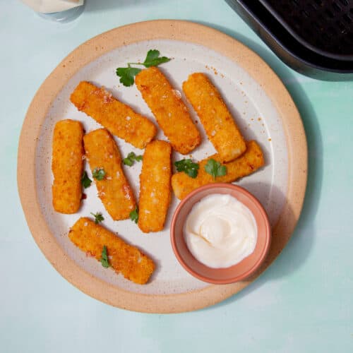 8 golden browned battered fish fingers on a plate with some mayonnaise in a small bowl and some fresh parsley.