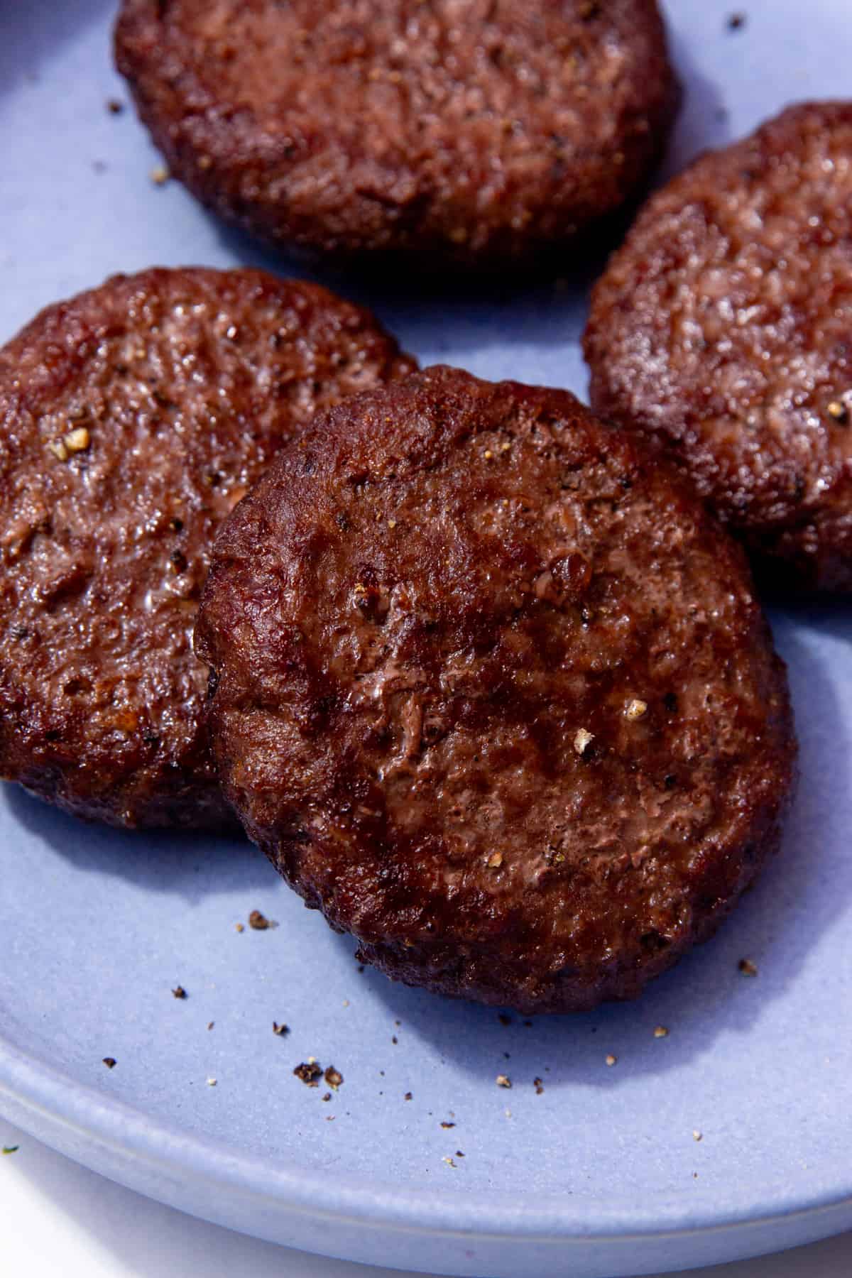 4 cooked, dark browned burgers on a blue plate.