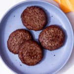 4 cooked, dark browned burgers on a blue plate with some cheese slices in the background.