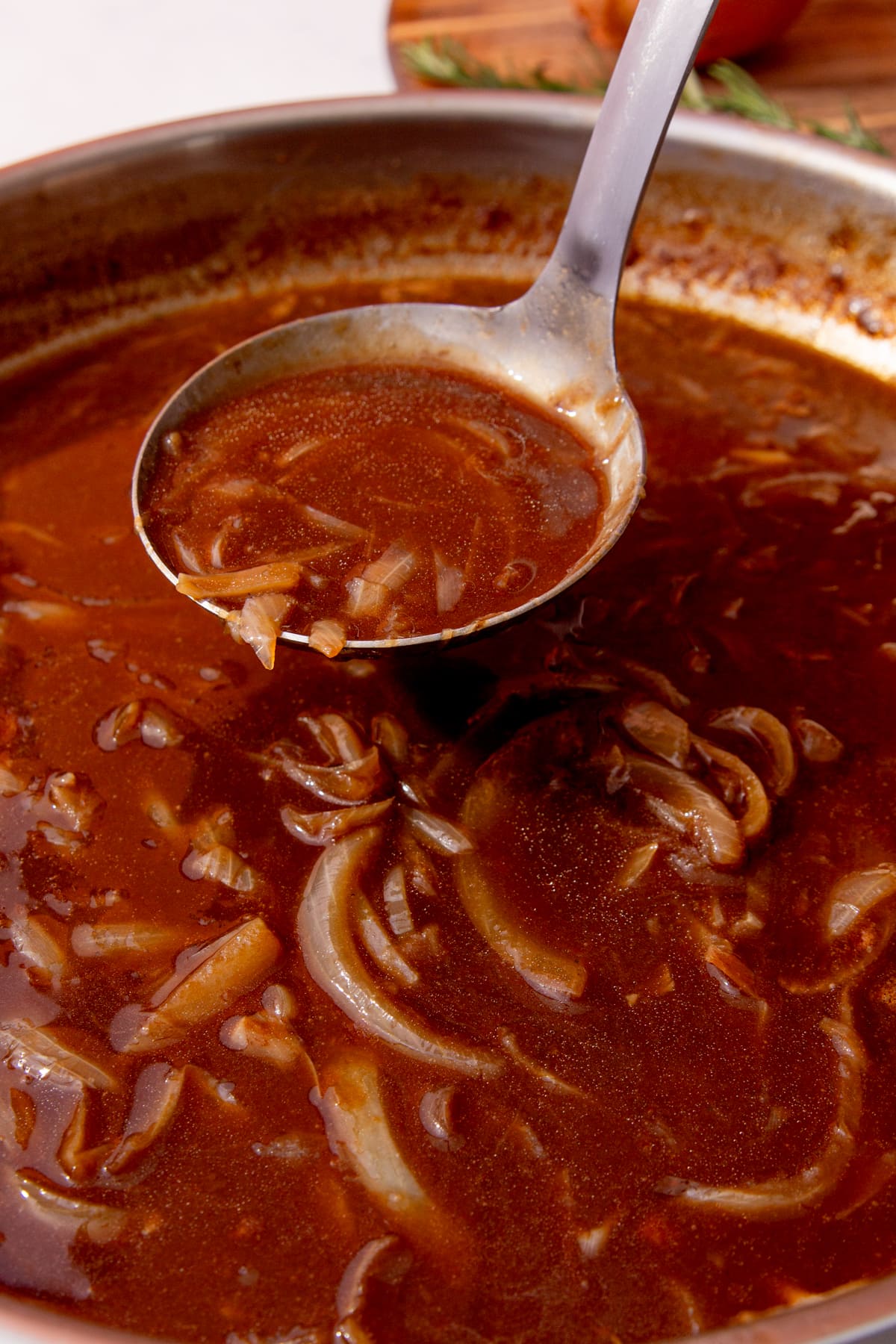 Gravy with onions in a large metal pan with a ladle filled with gravy and onions.