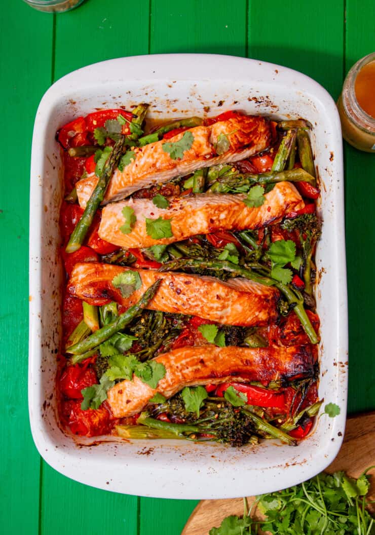 A white tray with baked salmon, and asparagus with other vegetables on a green background.