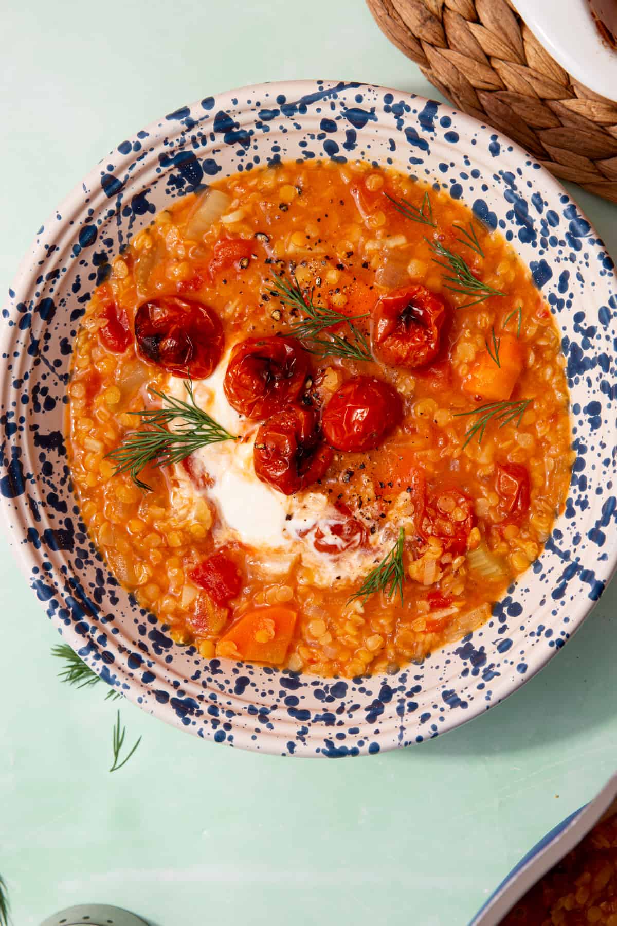 A patterned bowl full of red lentil soup with roasted cherry tomatoes, some dill and a dollop of creme fraiche.